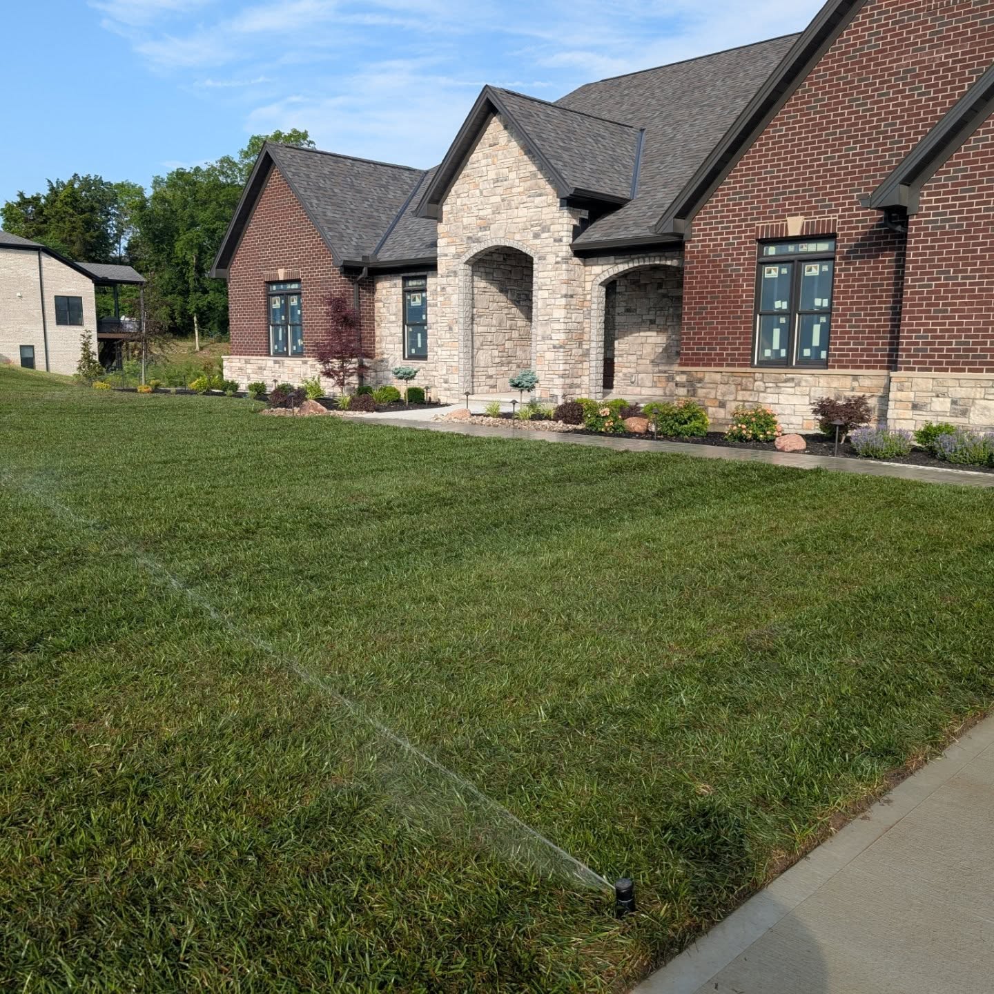 Irrigation system in residential lawn with sprinkler watering green grass near stone and brick house.