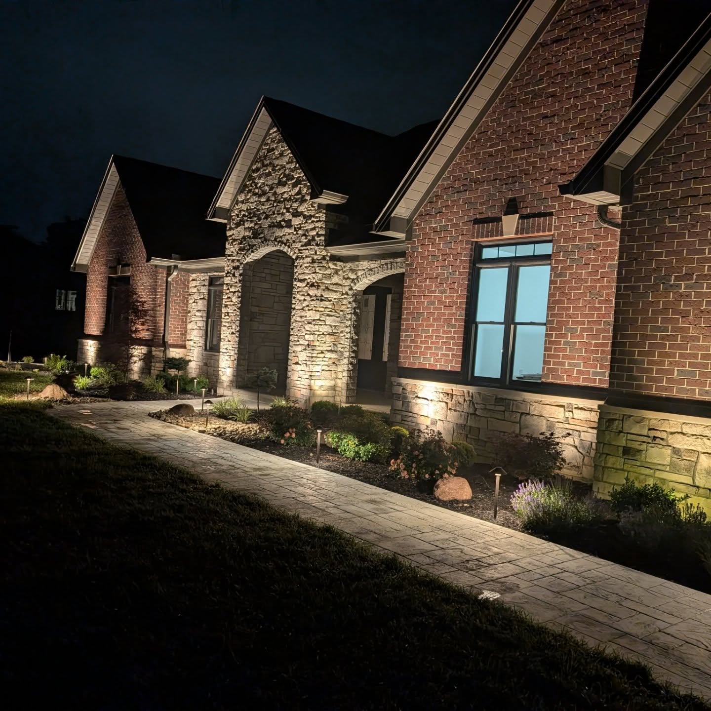 Outdoor lighting illuminating a brick and stone home in Northern Kentucky, highlighting architectural features and landscaping at night.