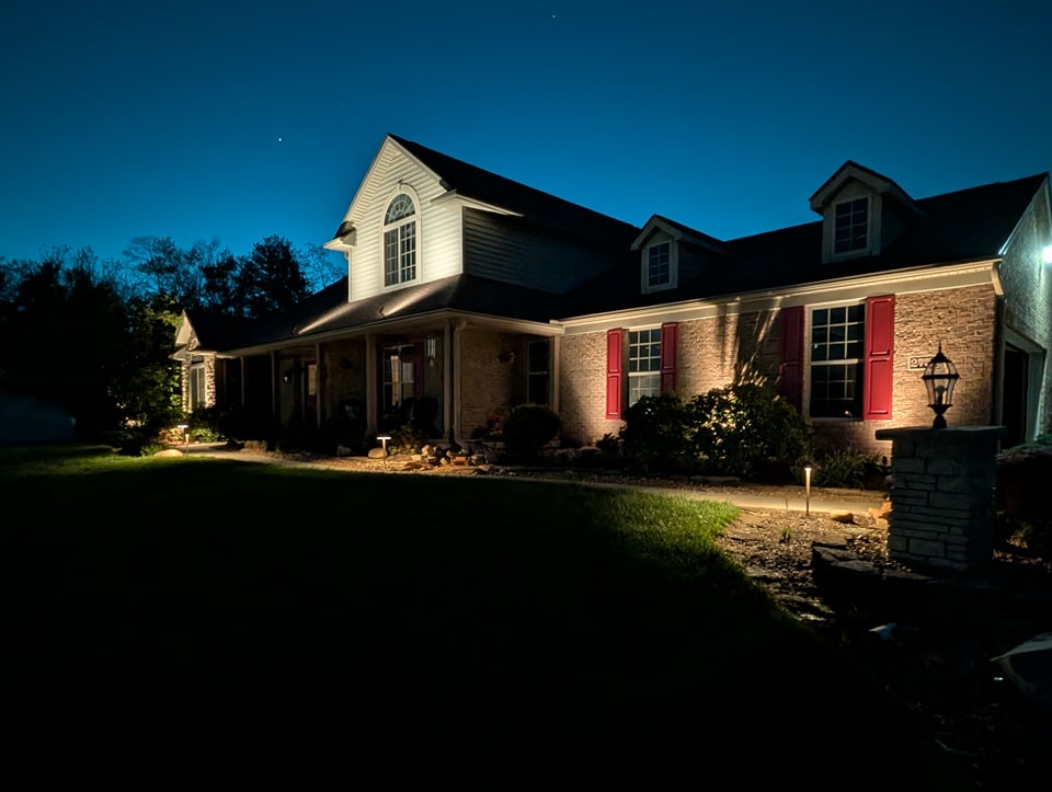 Outdoor lighting illuminating a brick home with red shutters and landscaped garden at night, enhancing curb appeal and safety in Northern Kentucky.